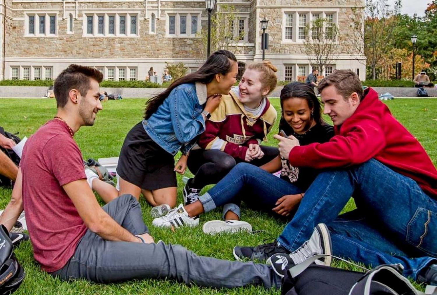 group of boston college students sitting and talking on the grass